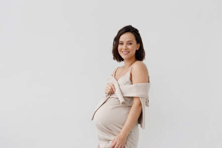 A young girl against a white wall with an empty space. Fashionable portrait of a happy pregnant woman in an elegant dress.の写真素材