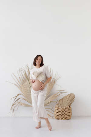A young pregnant girl in eco-style, on a white empty background. Smiling pregnant woman in boho...