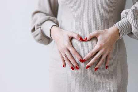 A young pregnant woman in a white dress, expecting a baby, hugs her stomach. Belly close-up, surrogacy.の写真素材