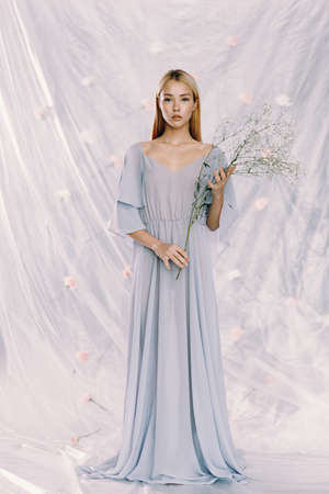 Portrait of a young beautiful girl in polyethylene with flowers on the background. Fashion portrait, environmental agenda.の写真素材