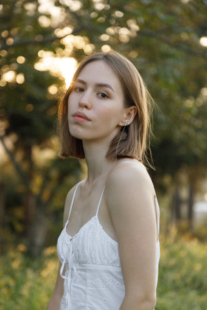 A young woman gazes thoughtfully while enjoying a sunlit outdoor setting, surrounded by the beauty...