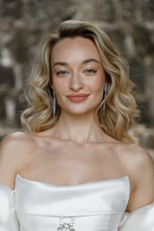 An Elegant Woman in a Beautiful White Dress with Soft Wavy Hair and a Radiant Smileの写真素材