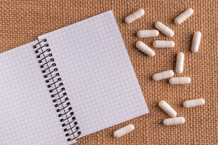 Medical capsules and pills around a blank notepad on a wicker background, close-up, top view, with copy space.の写真素材