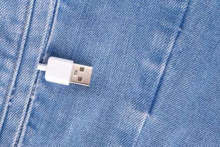 White USB cable connector in a denim pocket, the concept of communication and computer technology,...