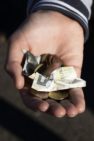 A child holds coins and euro notes in his hands. Pocket money image. Poor low-income family, the concept of poverty, beggingの写真素材