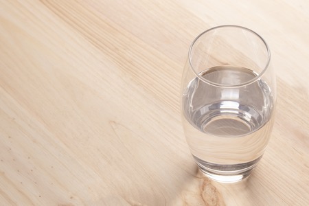 Image of a half full glass of water standing on a wooden tableの写真素材