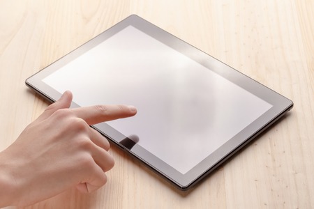 Hands use a black tablet on a wooden table, sunlit from the windowの写真素材