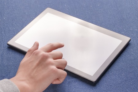 Hands use a brightly lit black tablet on a blue cloth sheet.の写真素材