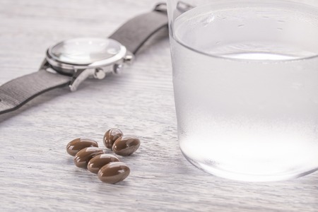 Misted glass of water and brown medical capsules on a white old wooden table. Wristwatches for proper medicationの写真素材