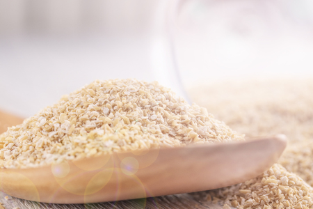 Oat bran in a wooden spoon and in a glass transparent glass on a white wooden table. The concept of healthy eating and sunny mood all dayの写真素材