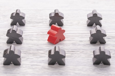 Uniqueness, individuality and difference. Red wooden figure in a crowd of different color on a white wooden table. The concept of disagreement with the majorityの写真素材