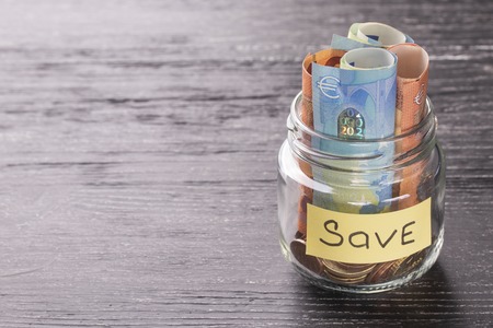 Euro notes and coins in a glass jar on a black wooden table with shiny reflection on a glossy surface. Money saving conceptの写真素材
