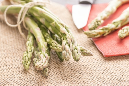 Fresh green asparagus on a table and in a white plate, tied with a rope, with a knife on a red napkin. Healthy food.の写真素材