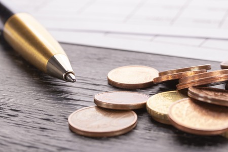 Stack of euro euro coins on old black wooden table. Pen and accounting documents with numbers. Payment planning utility billsの写真素材