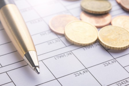 A pile of euro coins on an old black wooden table. Pen and accounting documents with numbers. Calculation of business successの写真素材