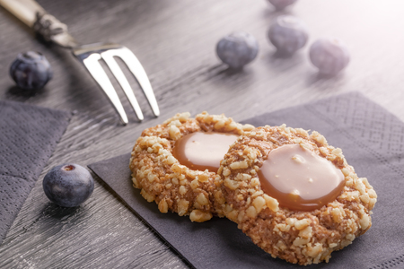 Peanut shortbread cookies with caramel jam inside on a black napkin with blueberries and a patterned dessert fork on a dark background nearby. Homemade dessert conceptの写真素材