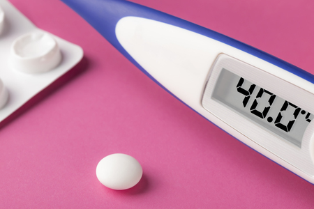 Electronic thermometer and pills on a pink background. High temperature 40 degrees Celsius on...