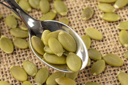 Shelled pumpkin seeds or pips on a dessert patterned spoon on a sack napkin. View from aboveの写真素材