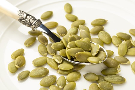 Peeled pumpkin seeds on a dessert spoon in a white plateの写真素材