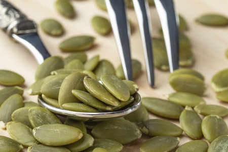 Pumpkin seeds in a dessertspoon on a wooden table close-up. The plug lies nearbyの写真素材