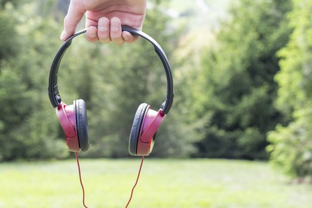 Red-black headphones in hand on the background of coniferous trees on the green grass and mountains in the distance. The concept of travel in nature and relaxation in the mountain parkの写真素材