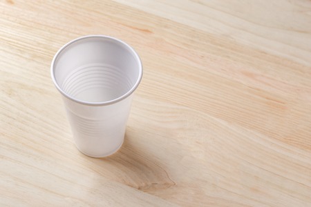 White plastic Cup stands on a wooden table of natural color. the concept of abandonment of plastic...