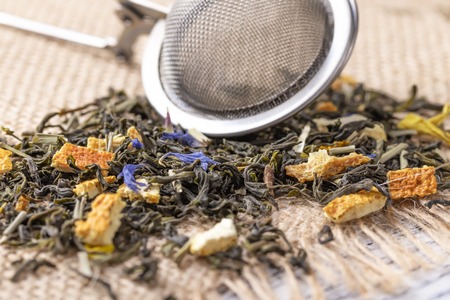 Green tea with orange peel and herbs with blue flowers. On a sackcloth with strainerの写真素材