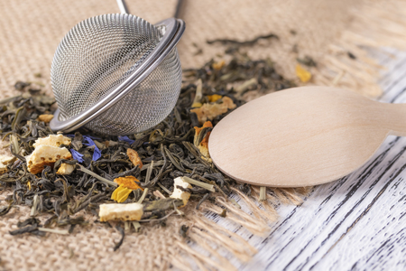 Herbal tea with blue flowers and orange peel in a wooden dessert spoon on sackcloth with strainerの写真素材