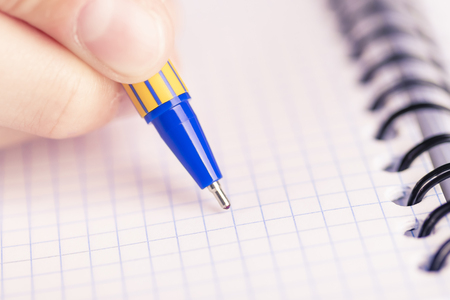 Man's hand with a black-gold pen over a clean sheet of checkered notebook. Spiral boundの写真素材
