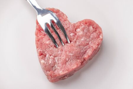 Juicy fresh minced meat patty on a beige plate. Fork with a pattern pierces it. Everything is ready to prepare good nutrition. Protein diet.の写真素材