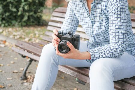 Girl in jeans and a shirt with a film camera in her hands in the park. Preparing for a photo shootの写真素材