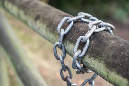 A metal chain is wound around a log gate in a park. The concept of strength and reliabilityの写真素材