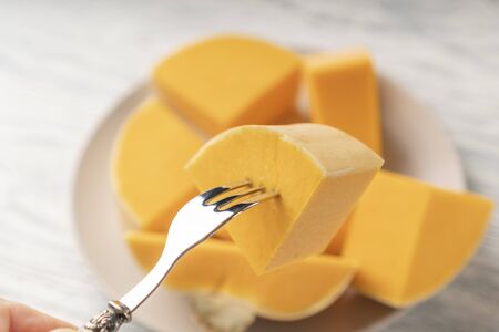 Fork with sliced ripe pumpkin on a beige plate on a white and black wooden table. Cooking Delicious...