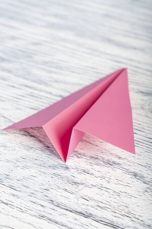 Pink paper airplane on a wooden white background. The concept of exciting travelの写真素材
