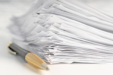 A pile of paper sheets on a white table on a wooden table with a golden pen. The concept of...