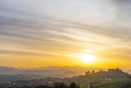 Sunset among the mountain peaks and wooded hills near the city. Cirrus golden and orange clouds....