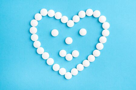 Heart shaped smile made from white medical pills on blue paper background. The concept of sedative...