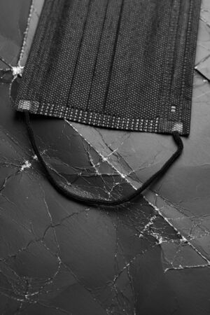Black medical mask on black crumpled paper with wrinkles and folds. Disposable protective surgical mask. Copyspace. Coronavirus Preventionの写真素材