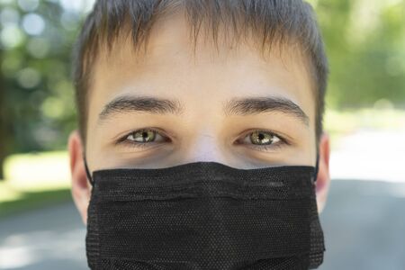 Sad young man in a medical black mask closeup near a road in a park. Close-up. The concept of coronavirus and quarantineの写真素材