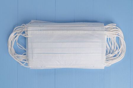 Stack of medical protective masks on a light blue wooden texture background close-up. View from...