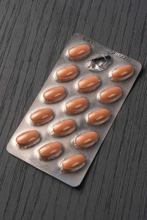 Close-up of packaging brown pills on a beautiful gray wooden textured background. One pill is...