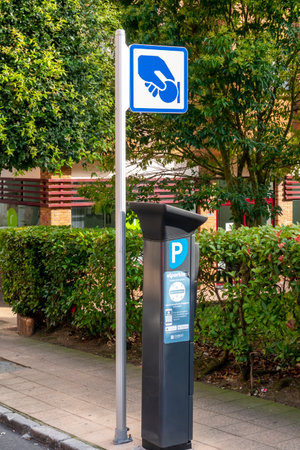 Oviedo, Spain, Asturias - August 2020: Parking payment machine with a blue sign symbolizing a hand holding a coin. On the street of the European Spanish city of Oviedo in the northern region of Spain, Asturiasのeditorial素材