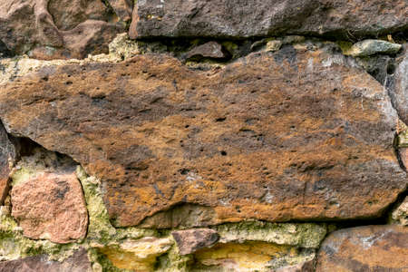 Stone brown wall made of natural weathered stones close-up