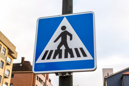 Pedestrian crossing road sign on the street close-up on a metal pillar fastened against the background of buildings and the sky. Road safety conceptの写真素材
