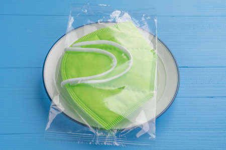 Protective respiratory mask in a transparent pack in a plate on a blue wooden table in the cafeteria. Restaurant setting during the  pandemic with a KN95 medical mask.の写真素材