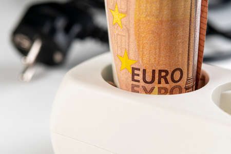 Fifty euro banknote in a white extension cord outlet on the background of wires and plug in blur. Macro. Home electricity purchase and budget saving efficiency conceptの写真素材