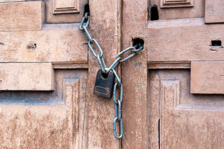 Rusty black padlock on a chain on an old vintage wooden closed door. Close-up. Entrance is a forbidden conceptの写真素材