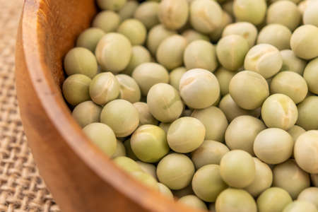 Dry green peas. Dried hard legumes in wooden rustic bowl on rustic rough sackcloth. Macro