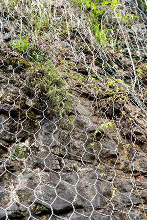 Natural rock with mesh to protect against landslides dangerously sliding down the cliff onto the...