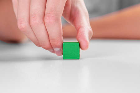 Hand moves green toy wooden block. Colored wood cube on a white table. Leadership and eco friendly...